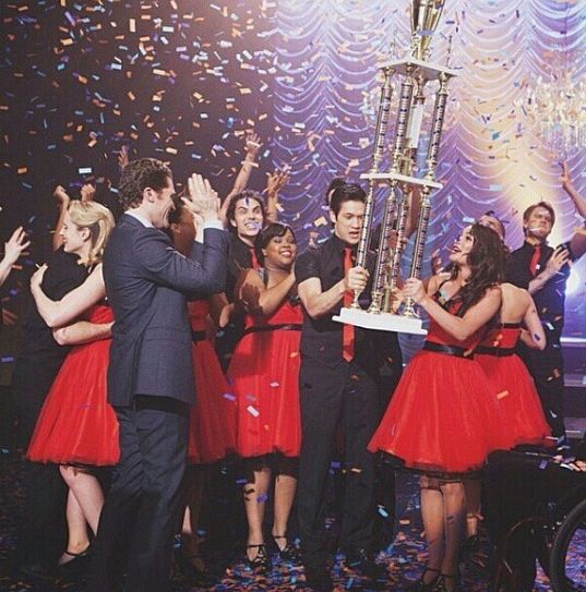 a group of people in red dresses holding up a trophy with confetti all around them