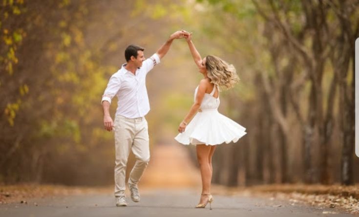 a man and woman holding hands while walking down the middle of an empty road with trees in the background