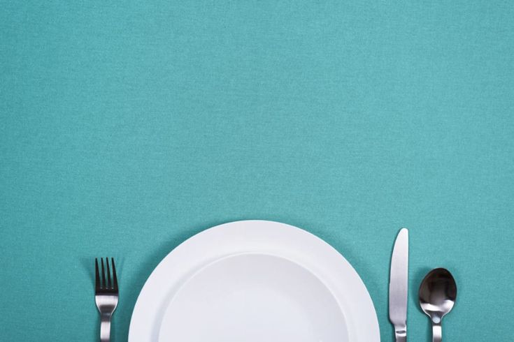 a white plate with silverware on it next to a knife and fork, against a turquoise background