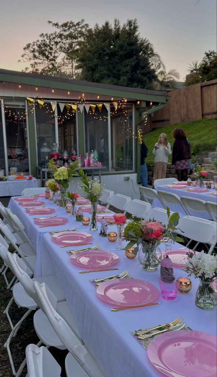 a long table set up with pink plates and place settings for an outdoor dinner party