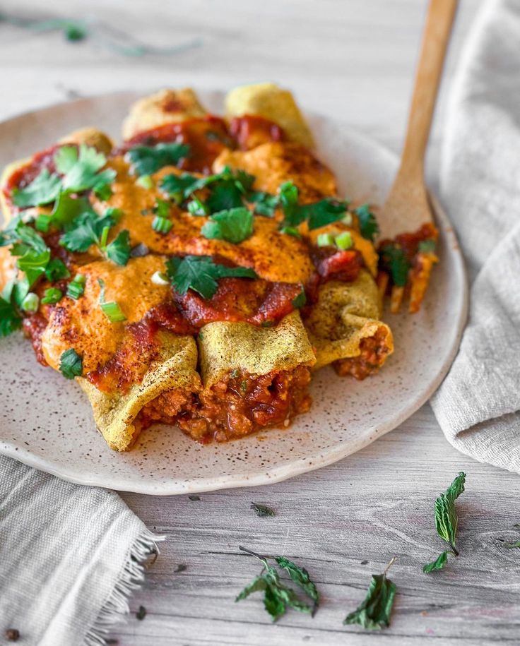 a white plate topped with lasagna covered in sauce and garnished with parsley