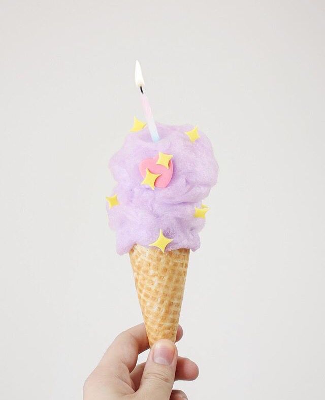 a hand holding an ice cream cone with a candle in it and stars on the top