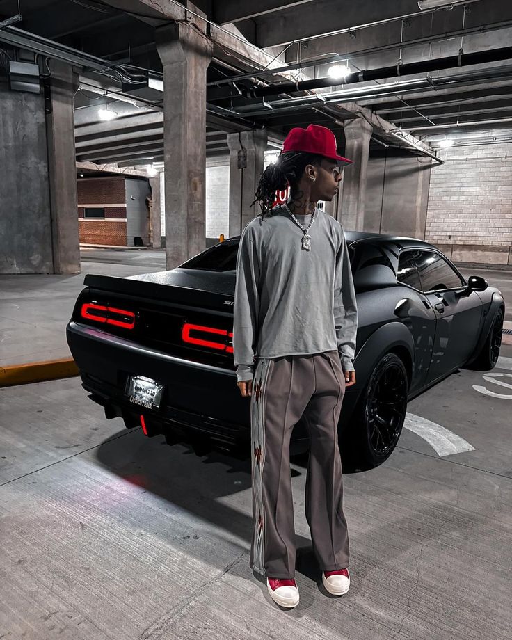 a man standing next to a black sports car in a parking garage with no one around