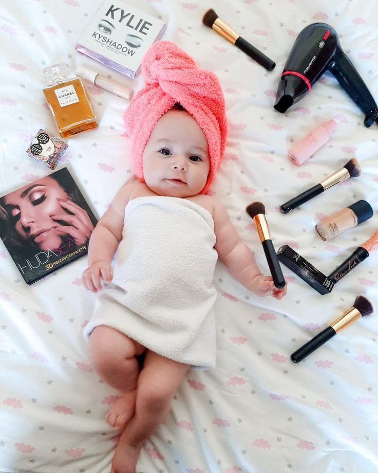 a baby laying on top of a bed next to makeup