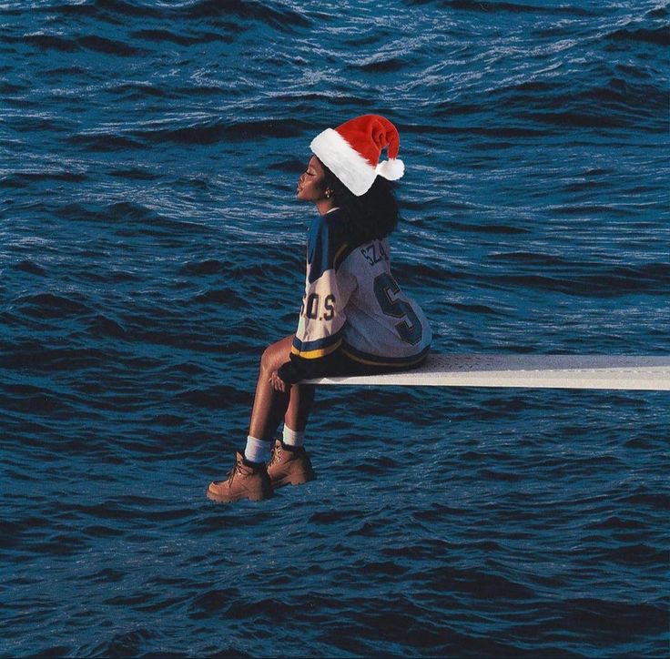 a young boy sitting on top of a boat in the ocean wearing a santa hat