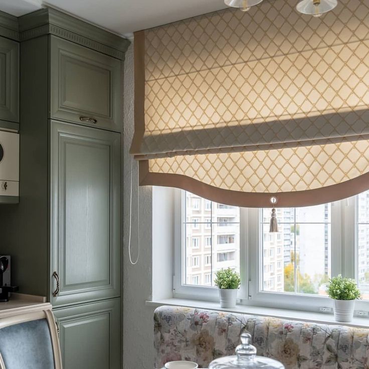 a kitchen with green cabinets and a window covered in roman blind shades over the windows