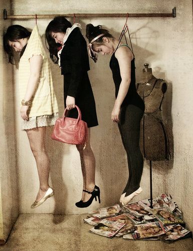 three women standing in front of a wall holding purses and looking at dresses on mannequins