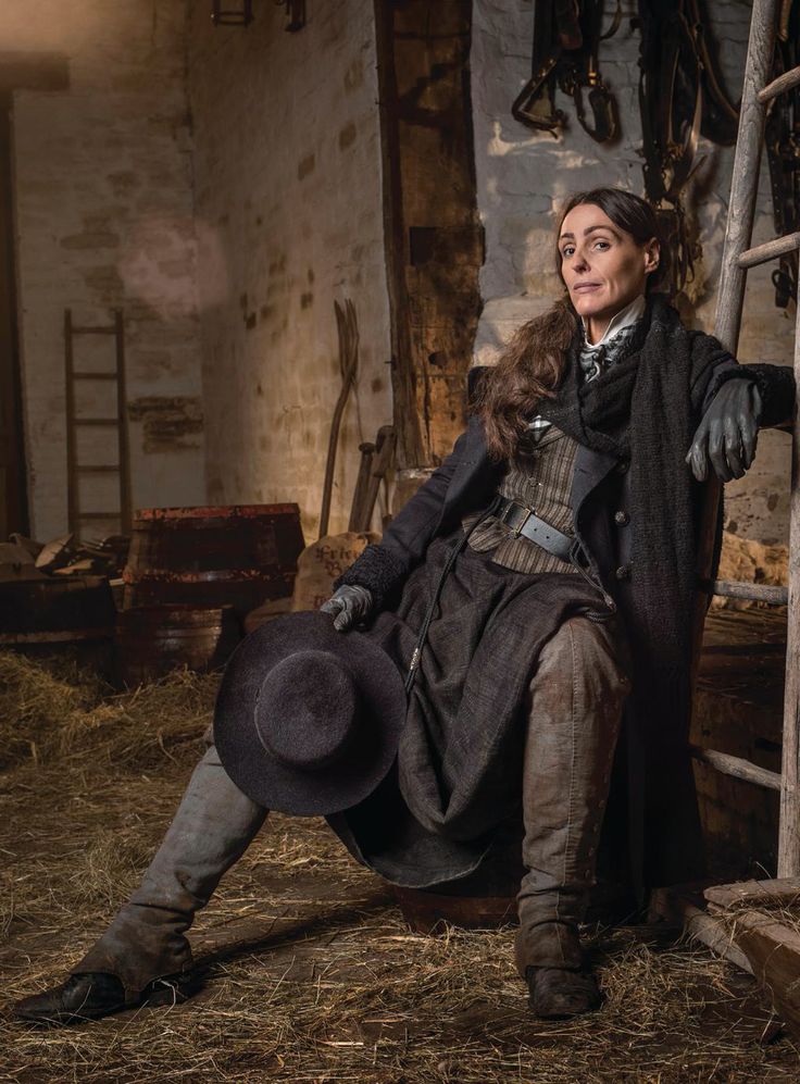 a woman sitting on top of a pile of hay next to a wooden ladder and holding a hat