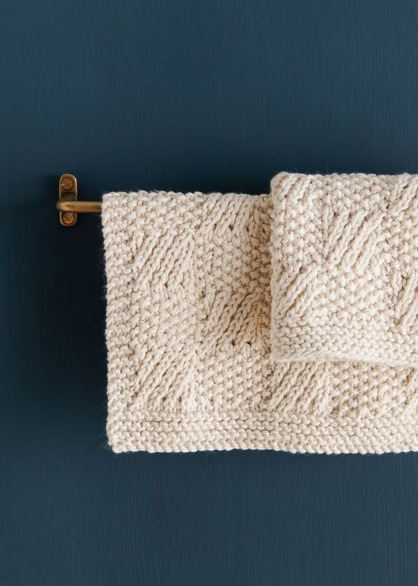 a white knitted towel hanging from a hook on a blue wall with a wooden handle