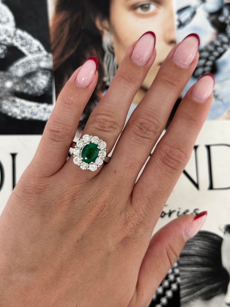 a woman's hand holding an emerald and diamond ring on top of her finger