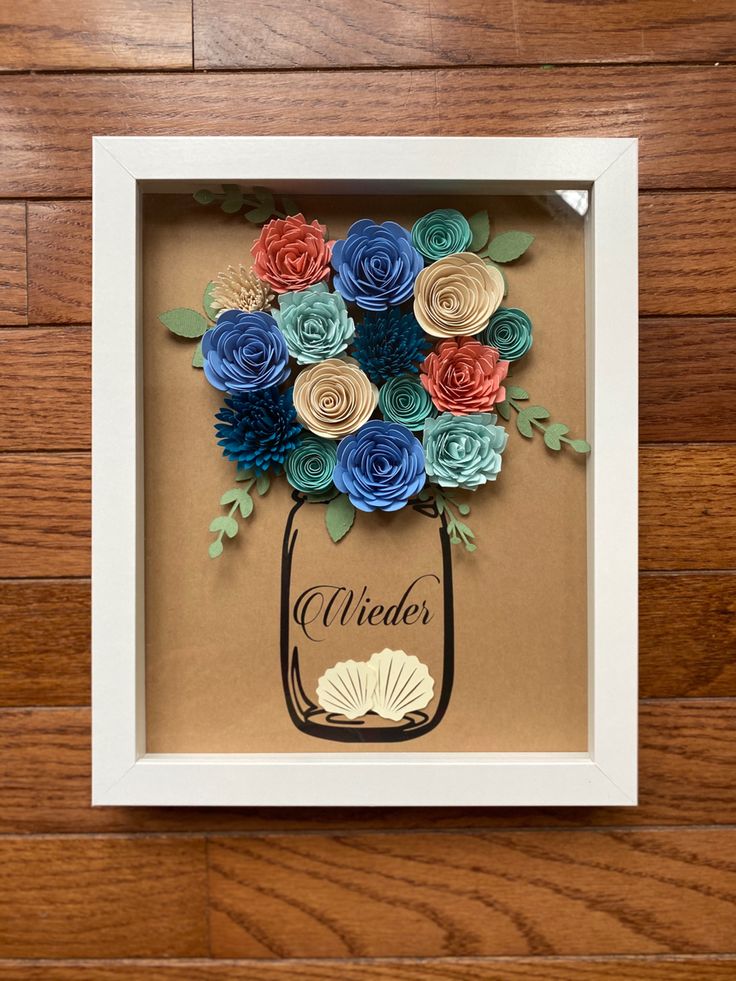 a paper flower arrangement in a frame on a wooden floor with the word wonder written below it