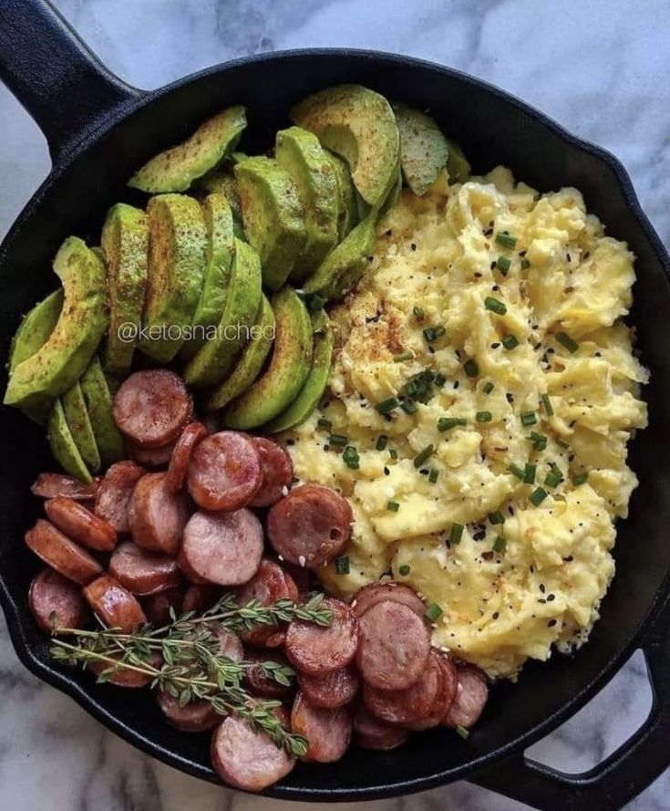 an iron skillet filled with eggs, sausages and avocados