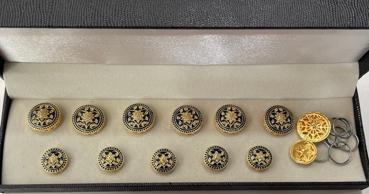 a display case holds nine pairs of gold and black buttons with designs on the sides