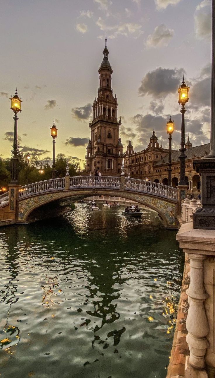 a bridge over a body of water next to street lamps and buildings in the background