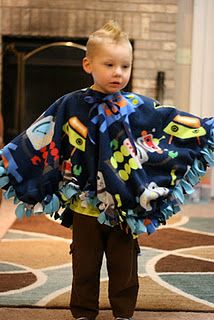 a little boy standing in front of a fire place with a blanket on his shoulders