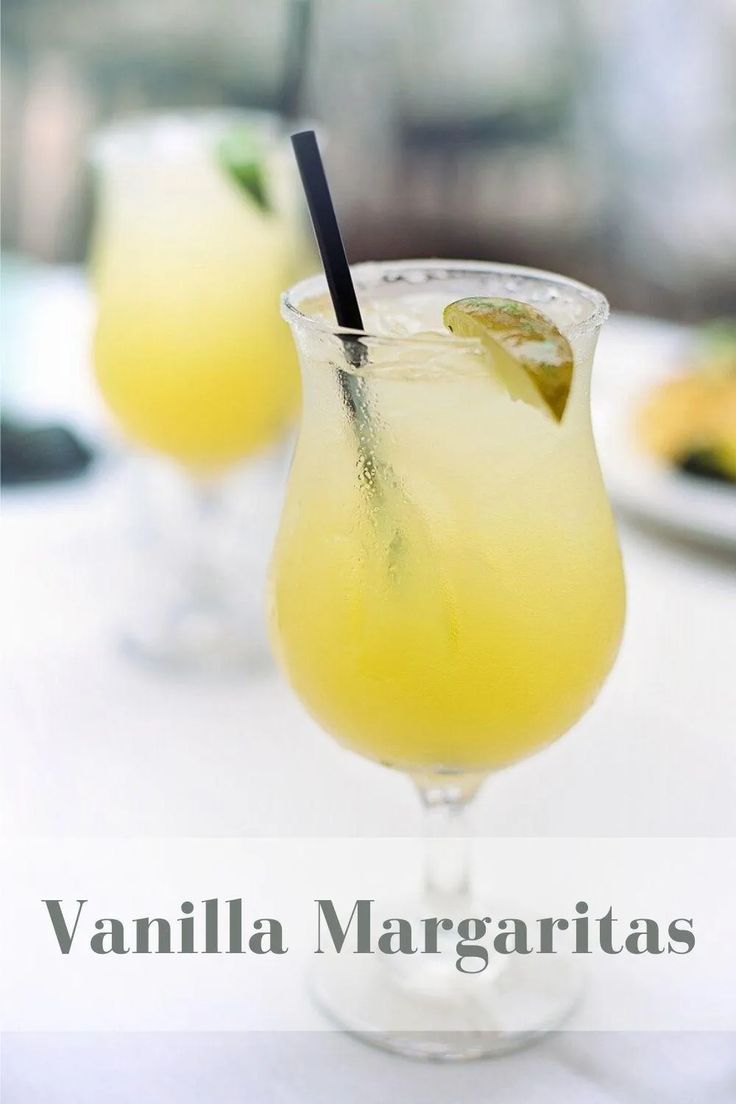 two glasses filled with yellow drinks sitting on top of a white tablecloth covered table