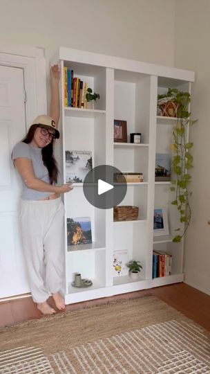 a woman standing in front of a white book shelf with books on it and an open door