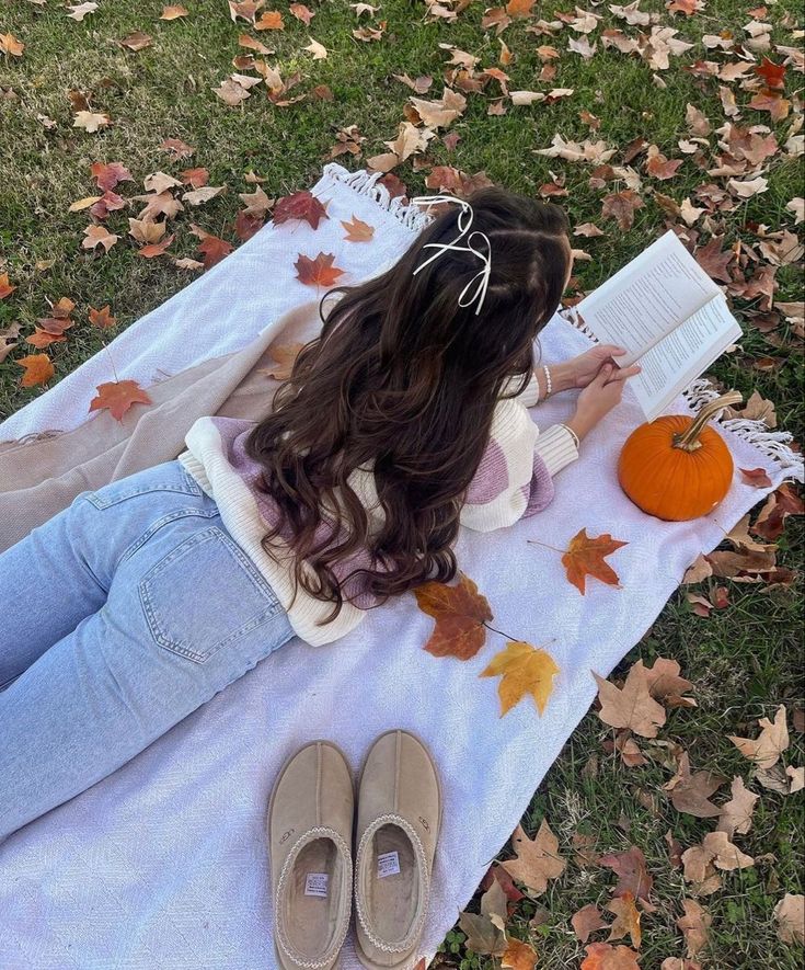 a woman laying on top of a white blanket next to a pumpkin and some leaves