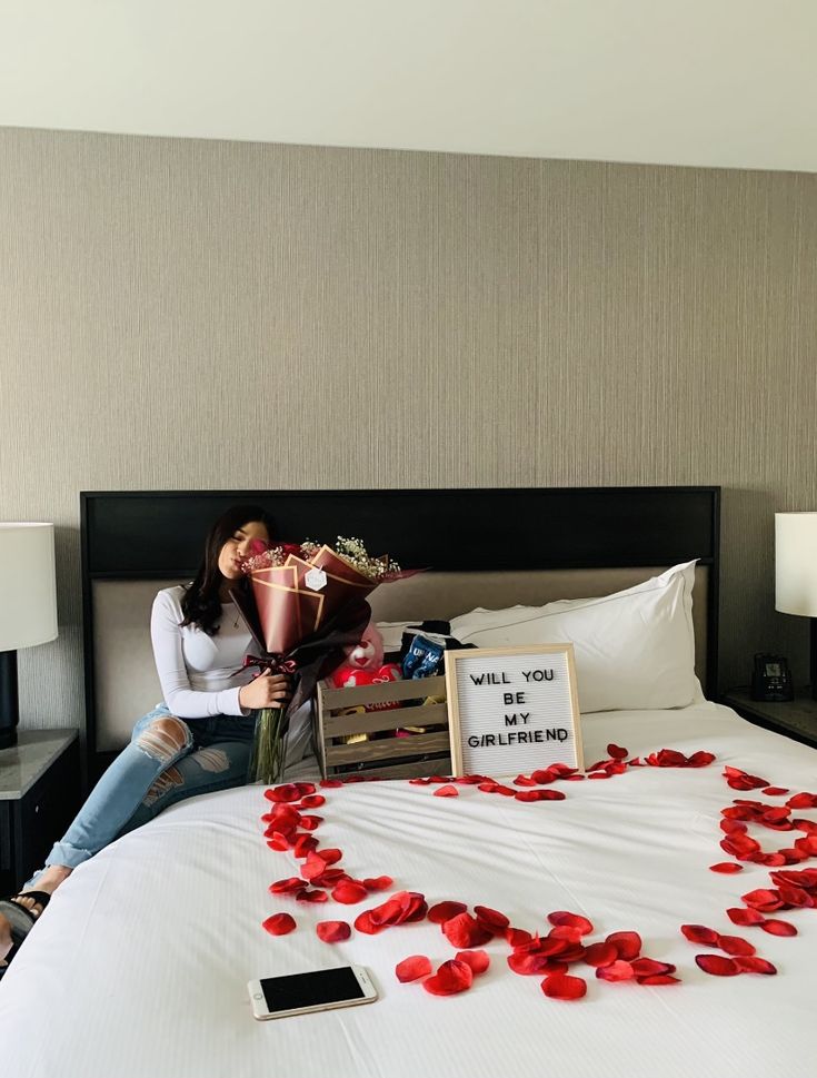 a woman sitting on top of a bed with rose petals in the shape of a heart