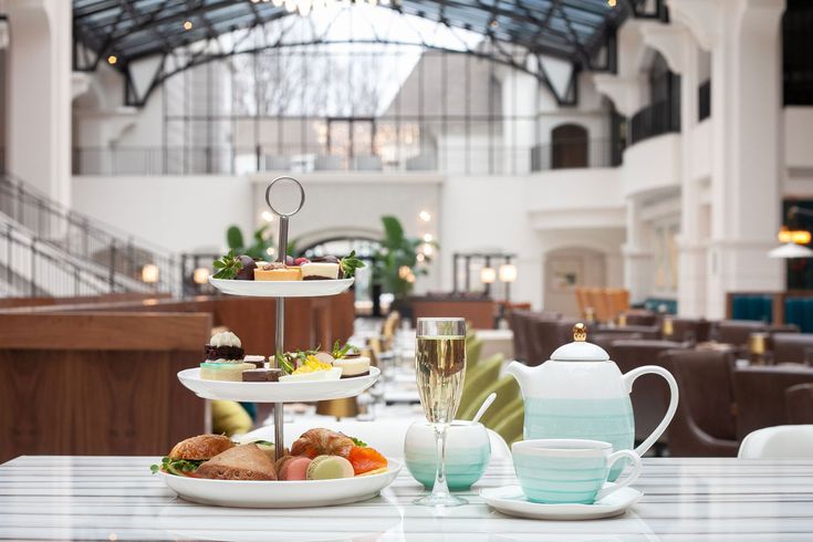 a table topped with three tiered plates filled with food next to cups and saucers