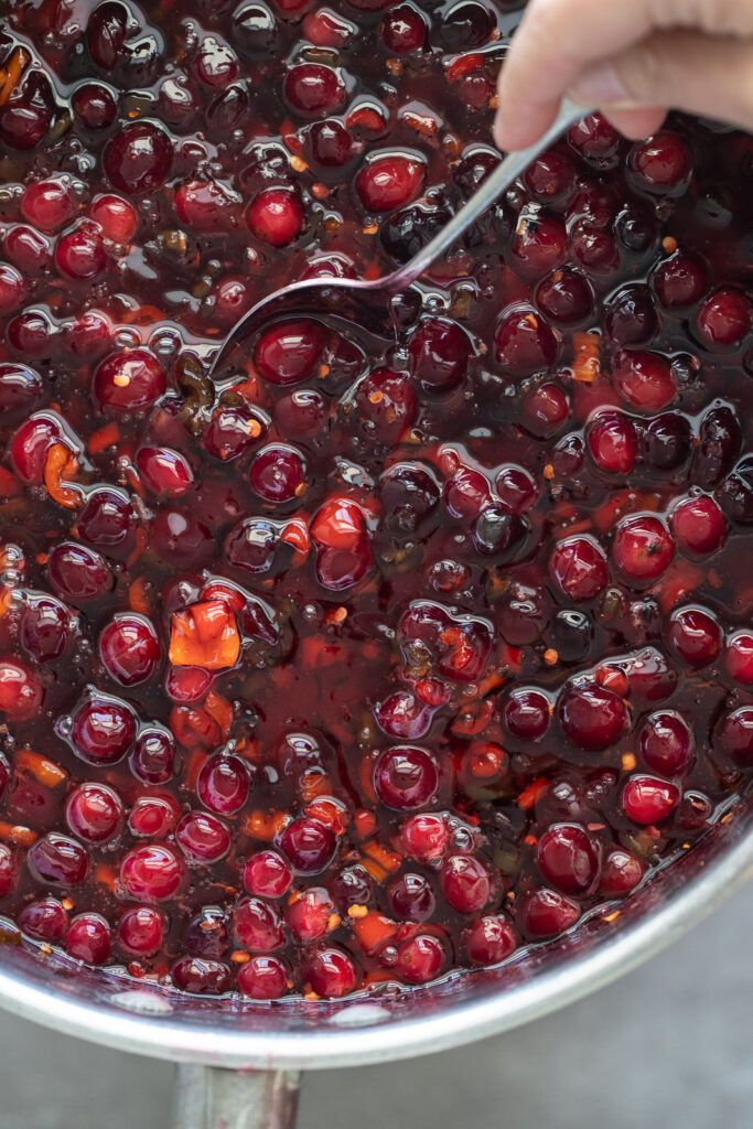 a person holding a spoon in a pot filled with cherries