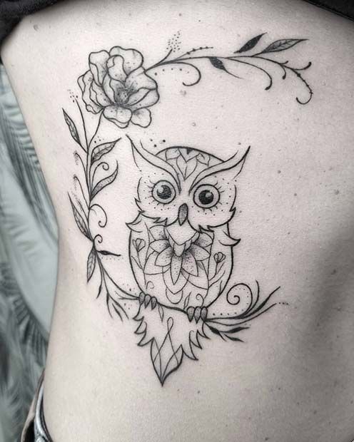 an owl tattoo on the back of a woman's lower body, with flowers and leaves around it