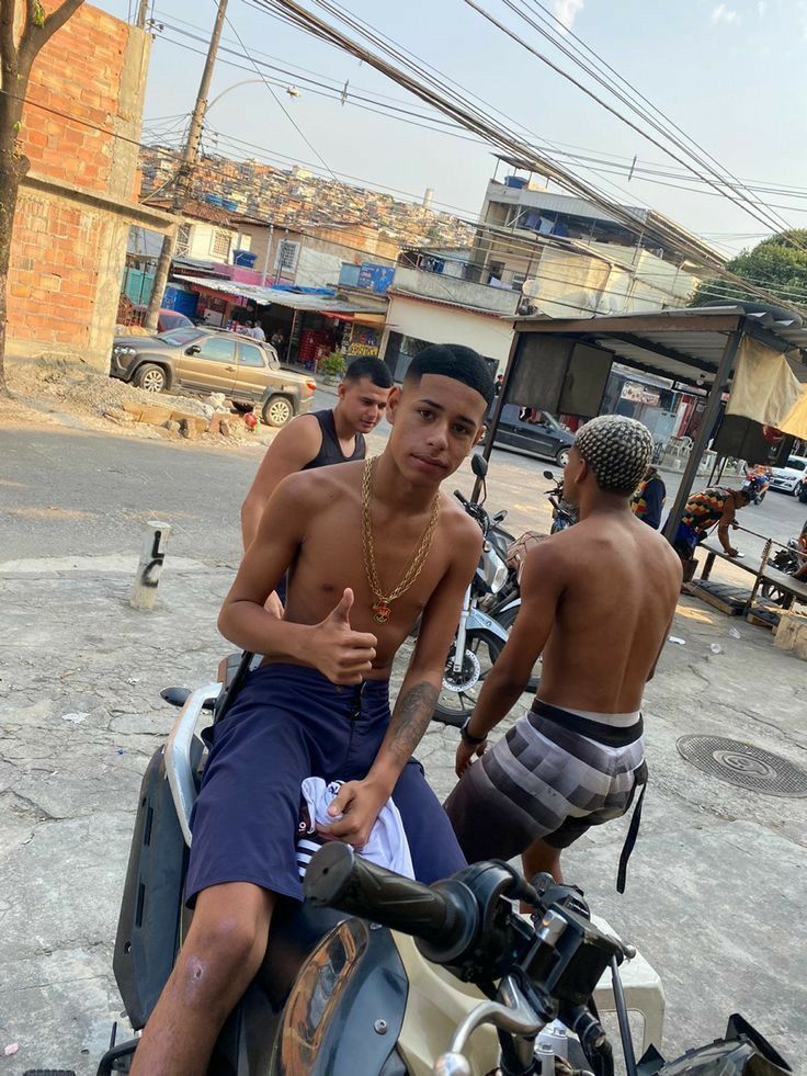 two young men sitting on the back of a motorbike with no shirt on