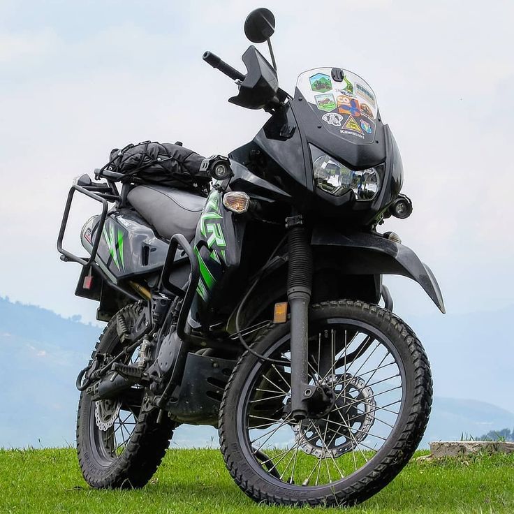 a motorcycle parked on top of a lush green field with mountains in the back ground