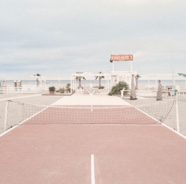 an empty tennis court on the beach with people in the background