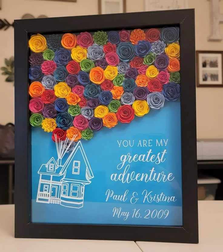 a picture frame that has some paper flowers in the shape of a house on it