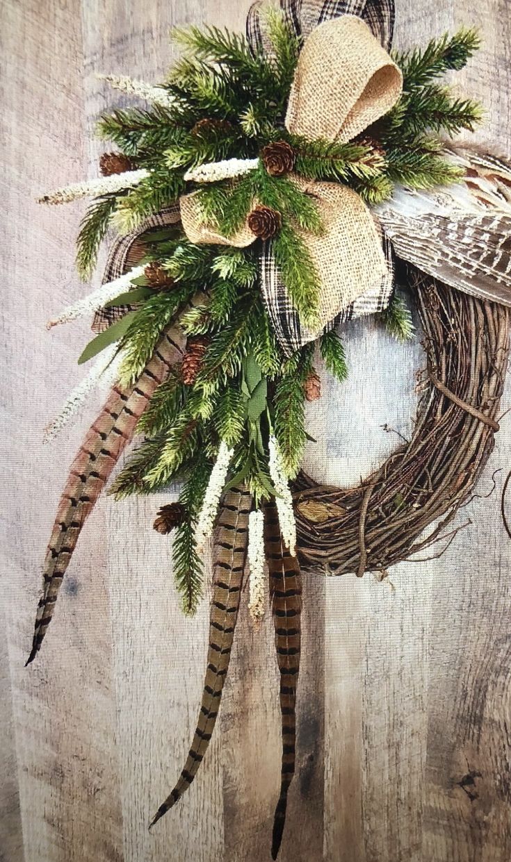 a wreath with feathers and pine cones hanging on a wooden wall