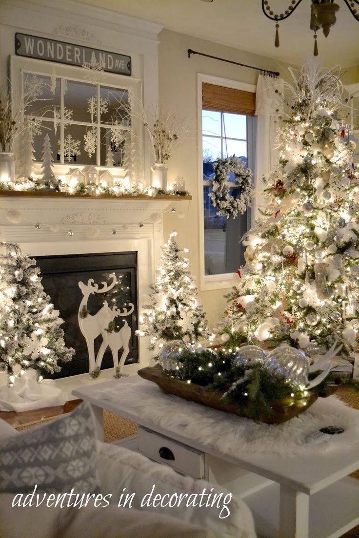 a living room decorated for christmas with white trees and other holiday decorations on the fireplace mantel