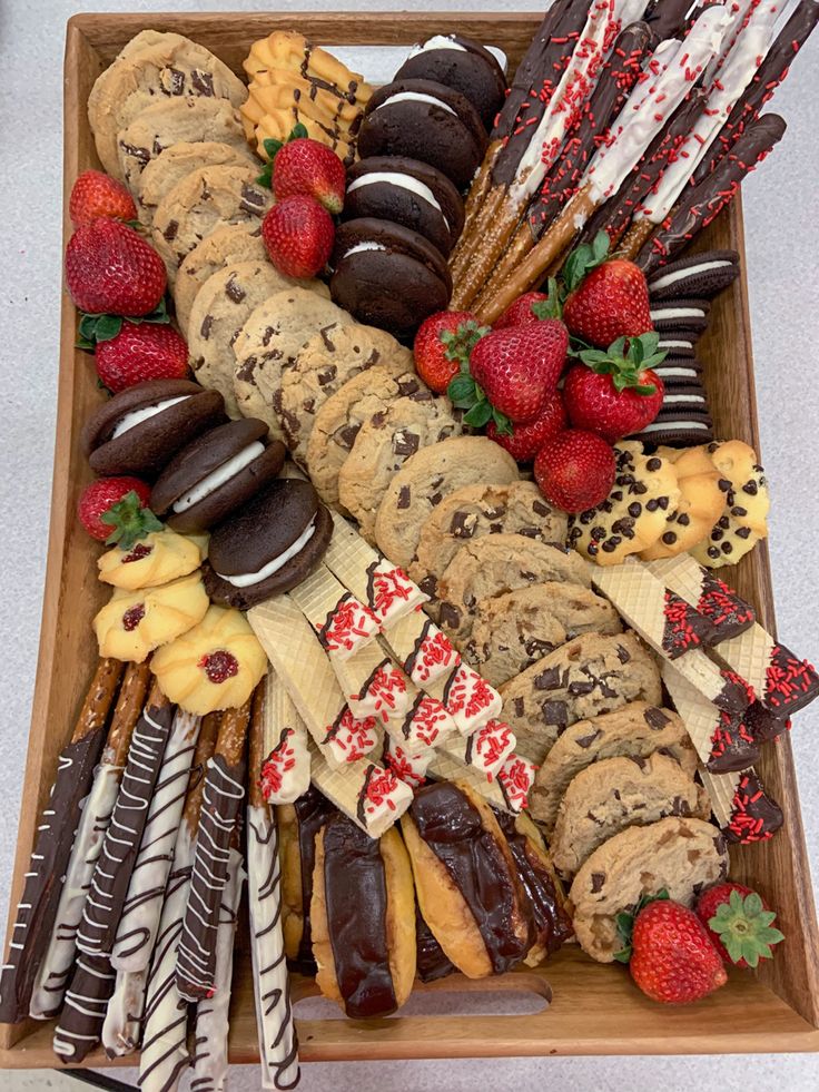 an assortment of cookies, strawberries and chocolates arranged on a wooden platter