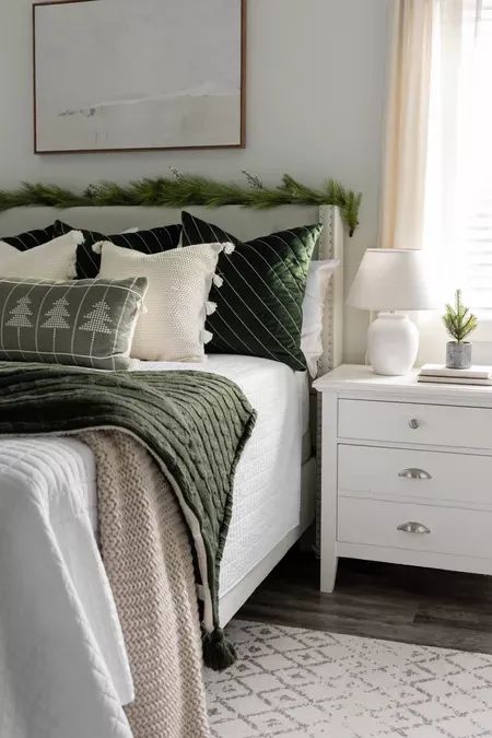 a white bed sitting next to a window covered in green and white pillows on top of a wooden floor