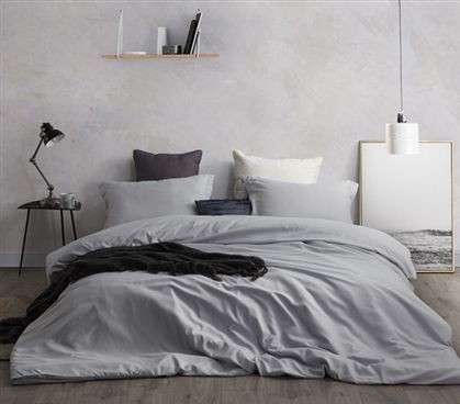 an unmade bed with grey sheets and pillows