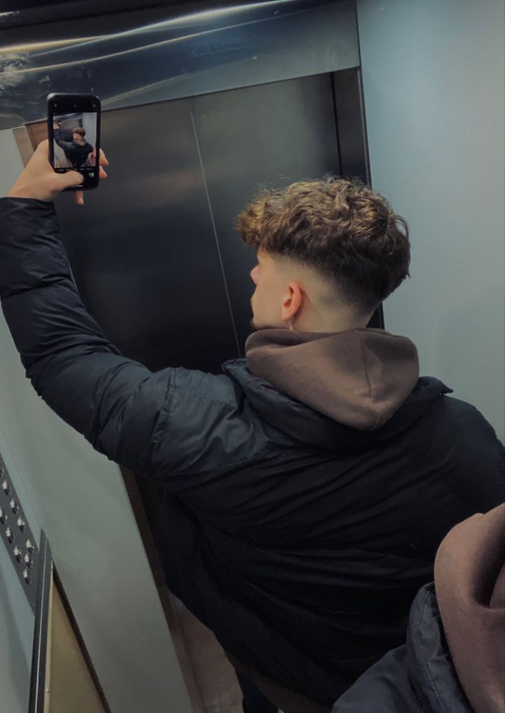 a man taking a selfie with his cell phone in front of an elevator door