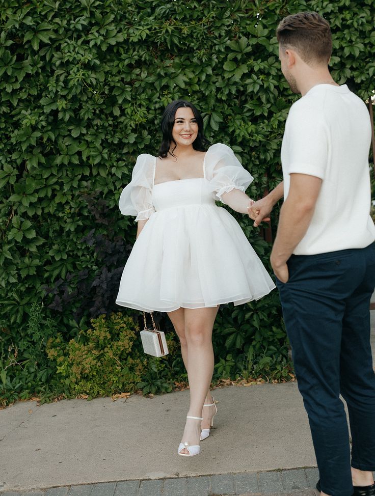 a woman in a white dress holding hands with a man