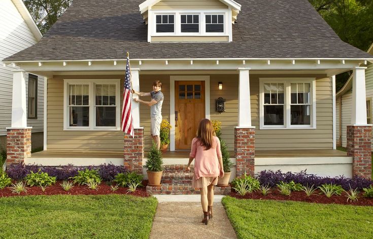 a woman walking towards a house with an american flag on the front door and a man holding a statue