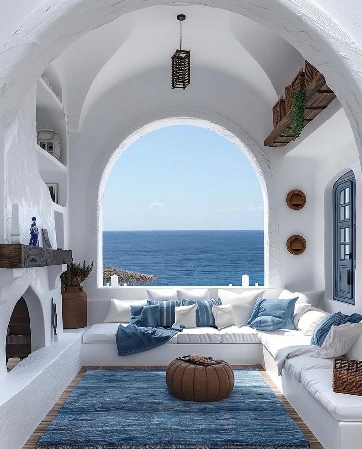 a living room filled with white furniture and an archway leading to the ocean in front of it