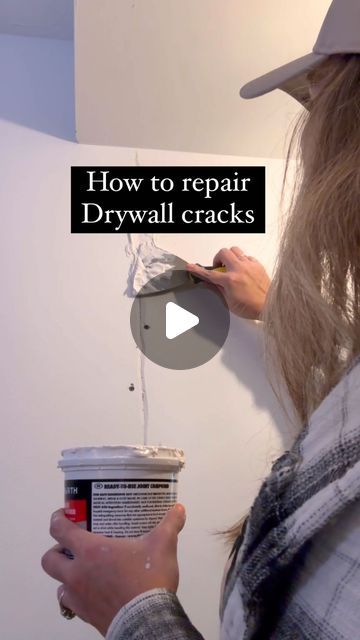 a woman is painting the wall with white paint and she is holding a can of drywall cracks