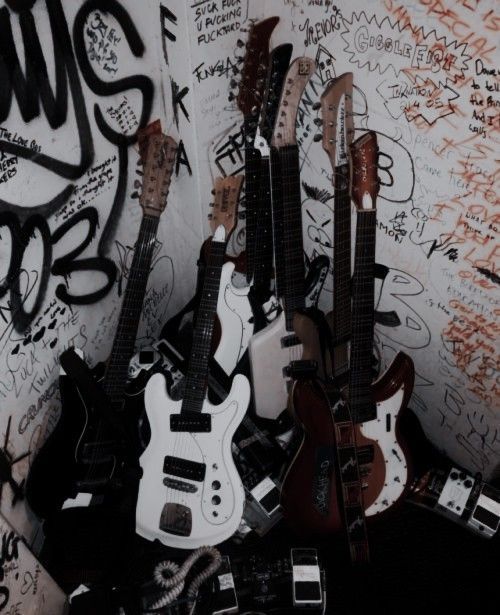 several guitars are lined up against a wall covered in graffiti