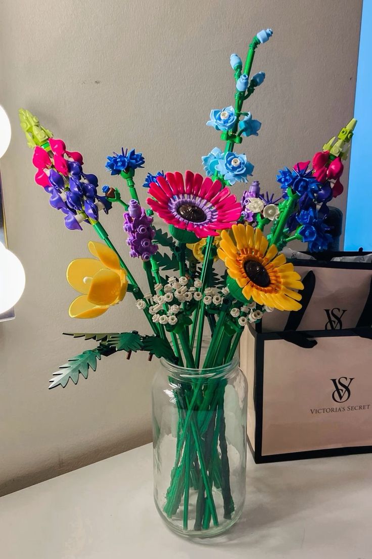 a vase filled with colorful flowers sitting on top of a table next to a bag