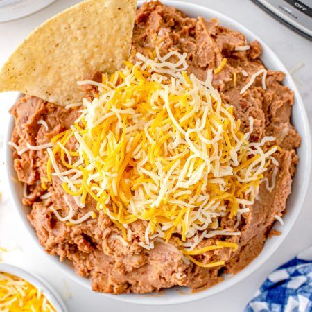 a white bowl filled with chili and cheese next to tortilla chips on a table