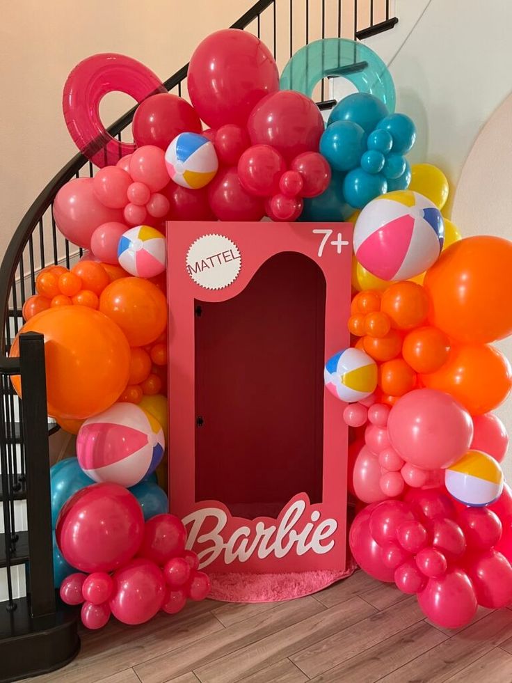 a bunch of balloons that are next to a fake barbie doll house with the door open