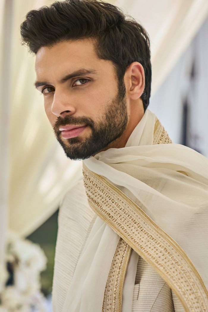 This cream sherwani set features all over gold zari embroidery on a raw silk base. It is paired with a cotton silk kurta and dhoti pants. Completing embroidered stole and footwear is also available.From Seema Gujral's Tuscan Summer collection. DELIVERY TIMEPlease allow 8-12 weeks for your outfit to arrive.FABRIC DETAILSRaw SilkProfessional cleaning only. Cotton Silk Sherwani With Chikankari Embroidery, Ceremonial Cotton Silk Bandhgala For Festivals, Traditional Cotton Silk Wear With Naqshi For Diwali, Traditional Naqshi Cotton Silk Wear For Diwali, Bollywood Cotton Silk Sherwani With Chikankari Embroidery, Ceremonial Cotton Silk Sherwani With Resham Embroidery, Ceremonial Cotton Silk Bandhgala With Zari Work, Cotton Silk Bandhgala For Ceremonial Eid, Festival Cotton Silk Sherwani With Resham Embroidery