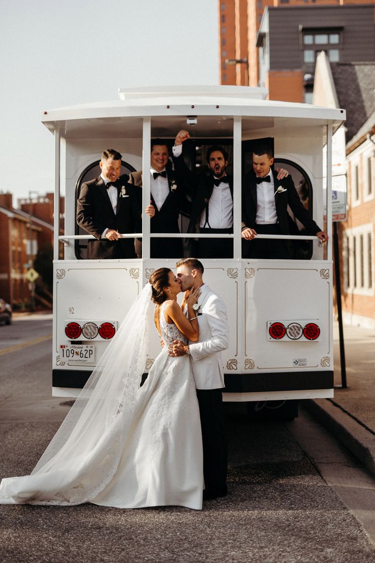 a bride and groom standing in front of a bus with their bridal party on it