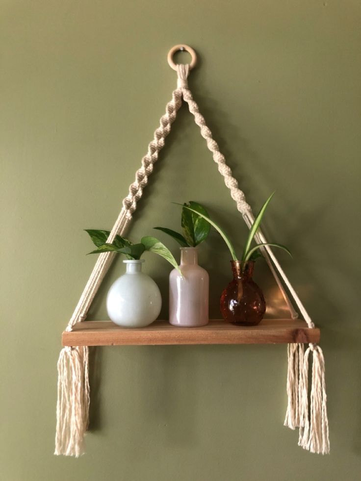 three vases are sitting on a shelf with rope hanging from the wall above them