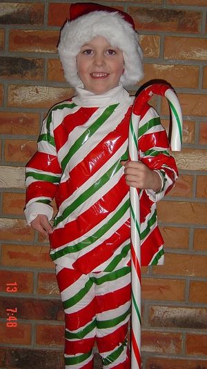 a young boy dressed as santa clause holding a candy cane in front of a brick wall