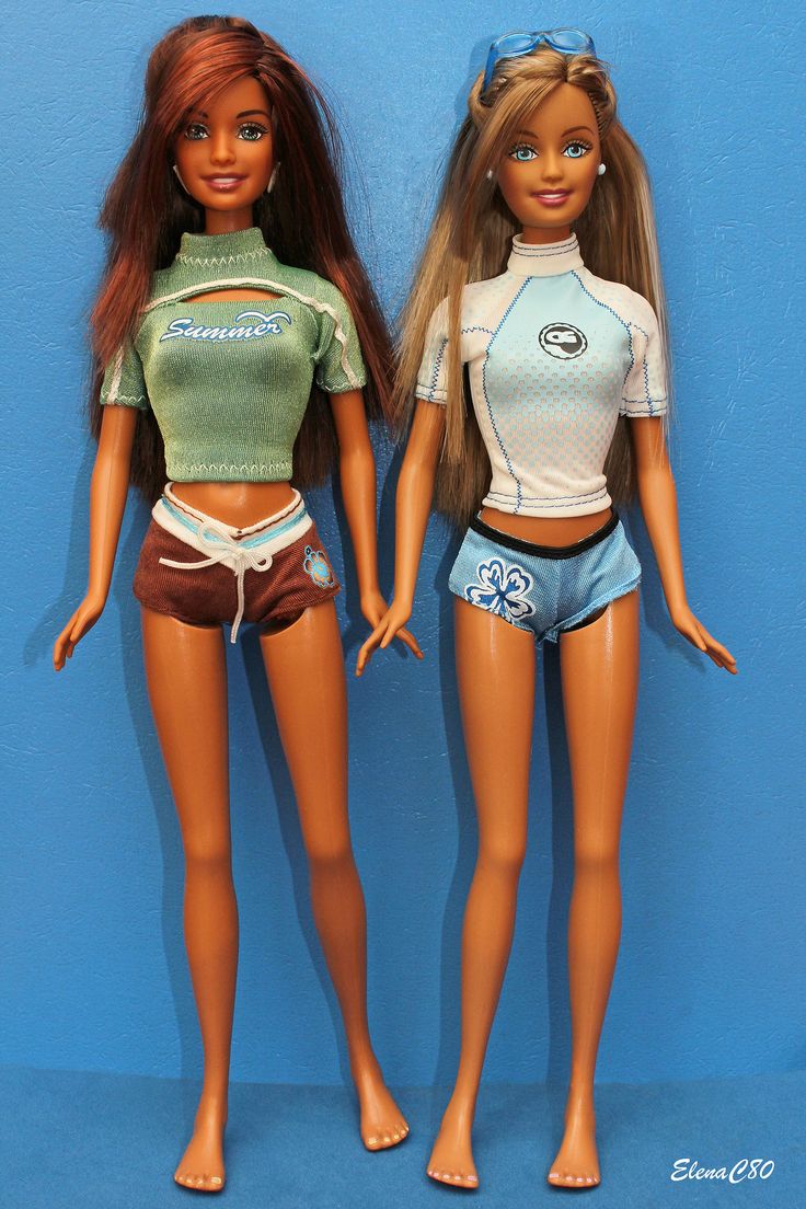 two dolls standing next to each other in front of a blue wall and one is wearing shorts