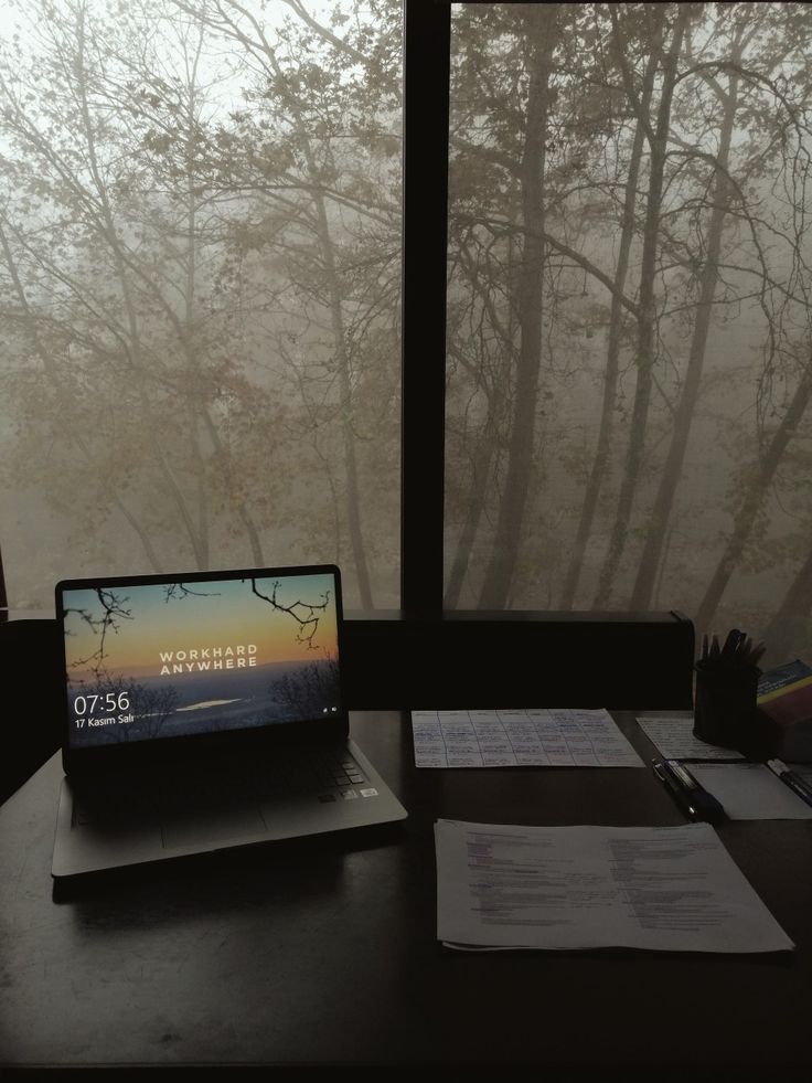 an open laptop computer sitting on top of a desk next to a window with trees outside